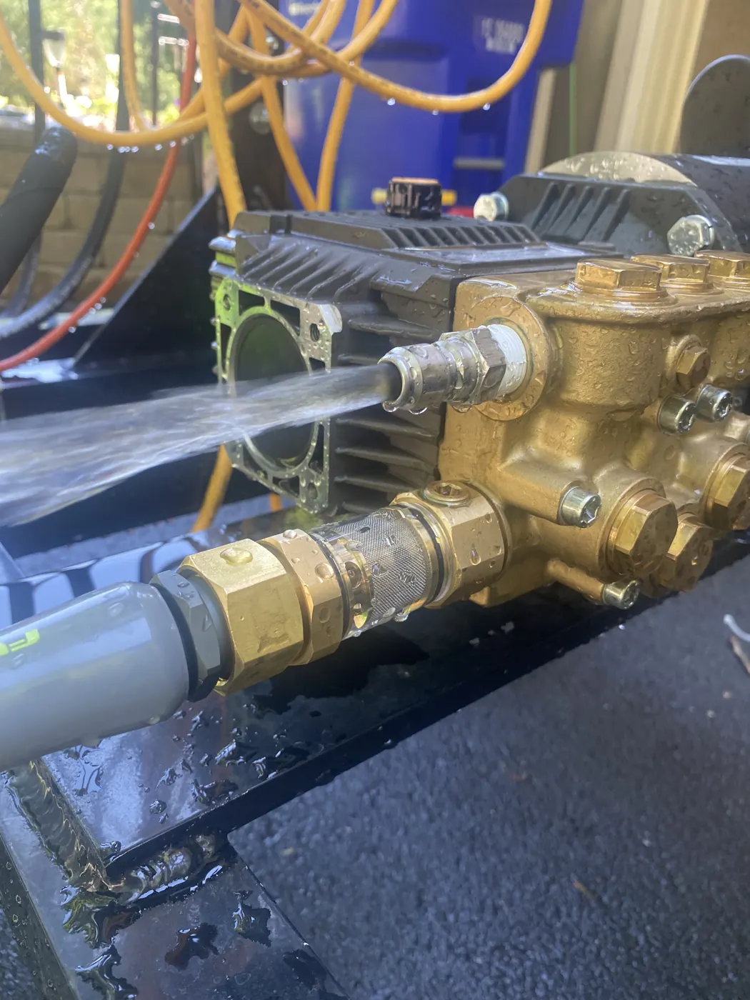 A brass triplex pump spraying water on a test bench.