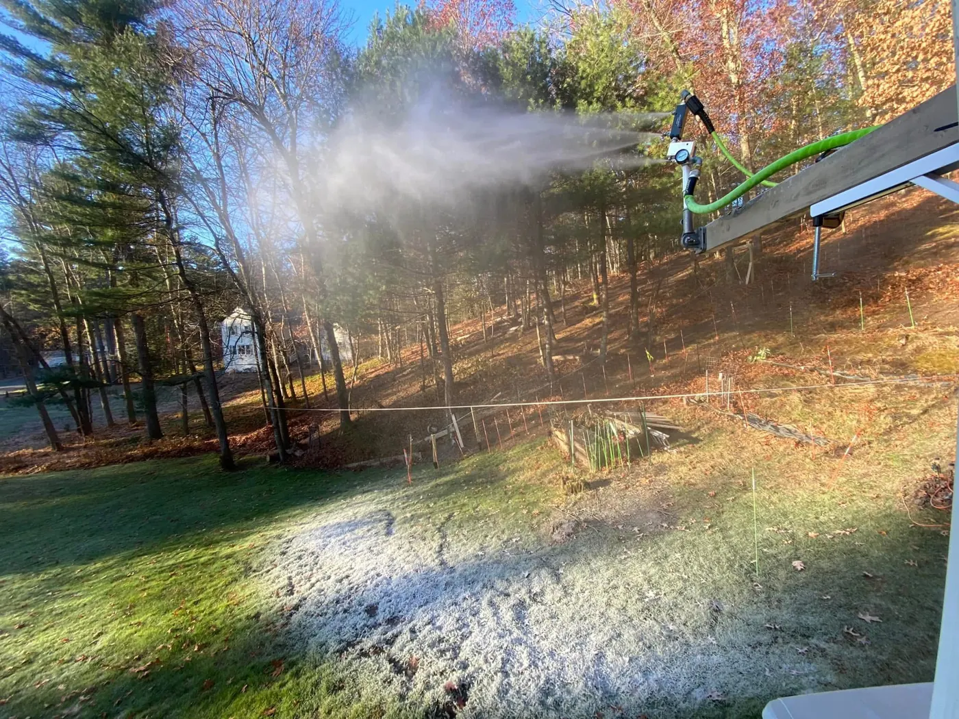 A snowgun on a boom firing snow across the yard, seen from above.