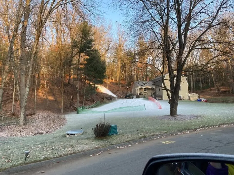 A snowgun throwing snow across the yard, seen from the street.