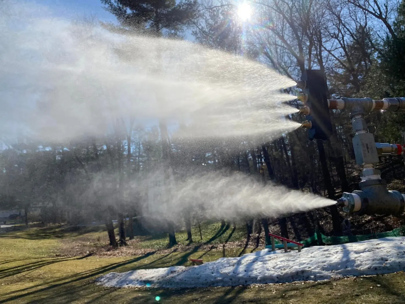 A snowgun throwing two plumes of snow into the sun.