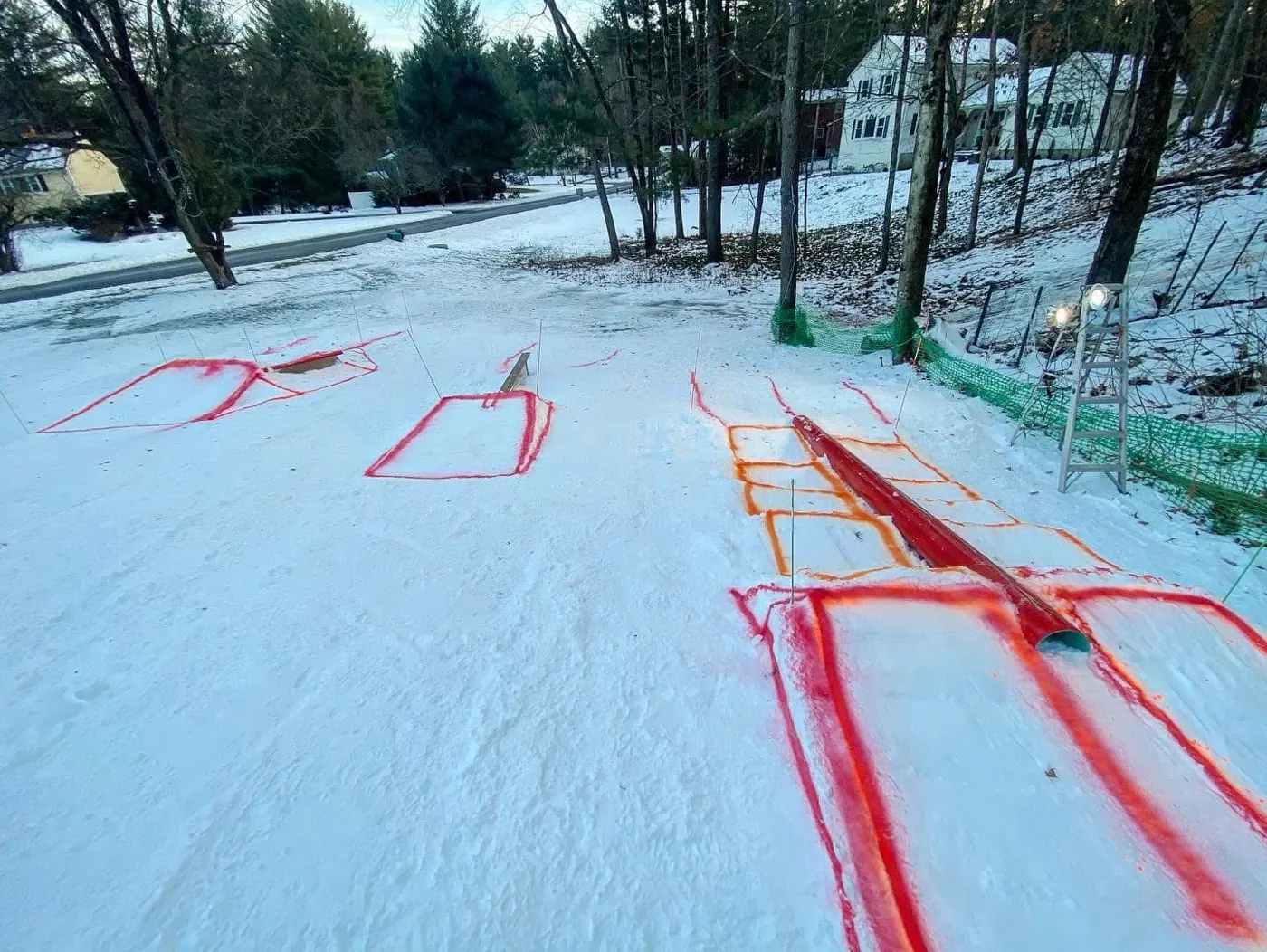 A terrain park on fresh snow with rails and boxes marked out in red paint.