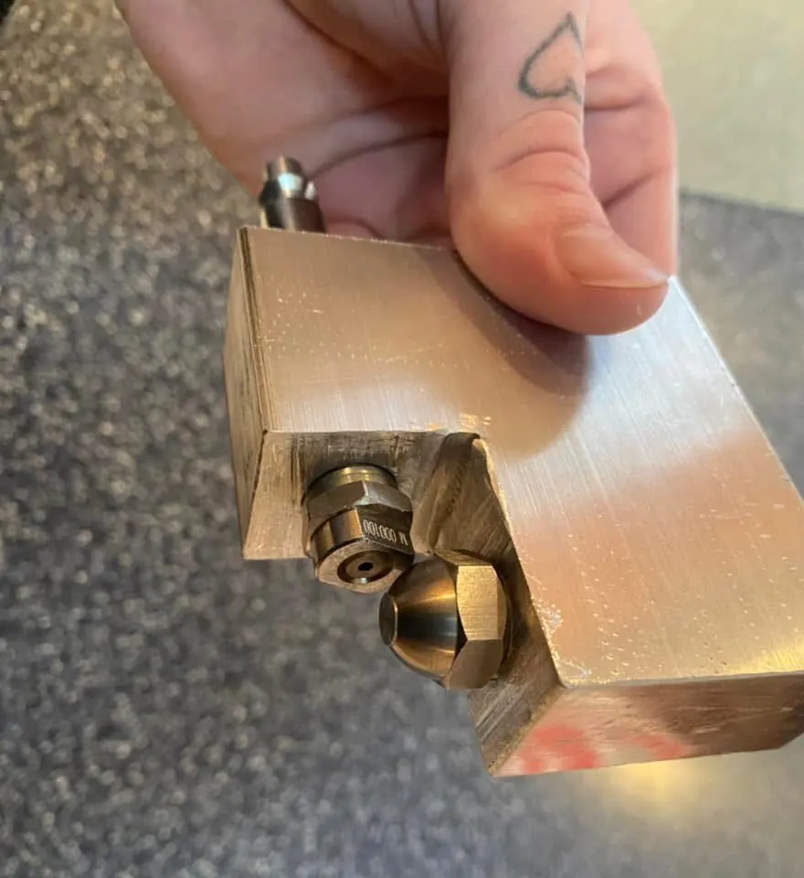 A machined nucleator block prototype with fittings, held in hand.