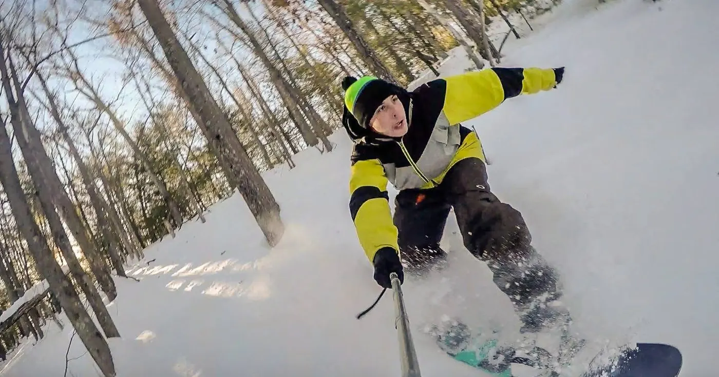 A snowboarder riding through powder with a pole camera.
