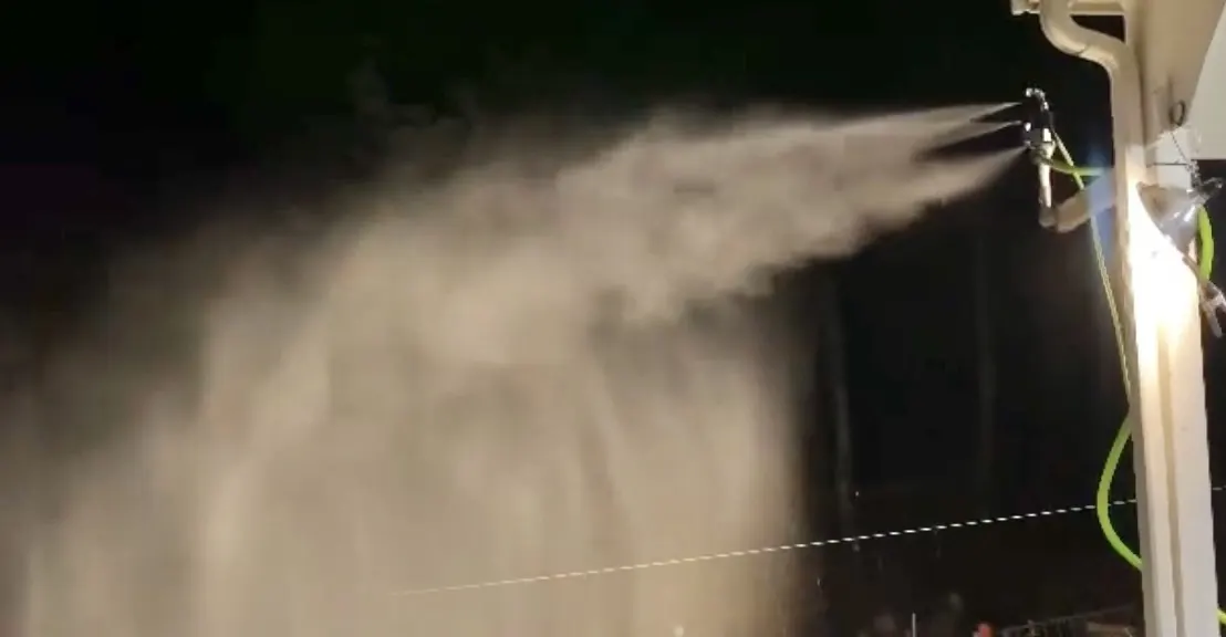 A snowgun mounted on the house firing a plume at night.