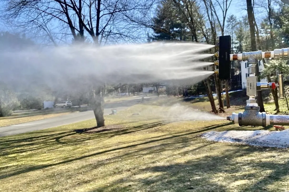 A multi-nozzle snowgun running in a sunny yard.