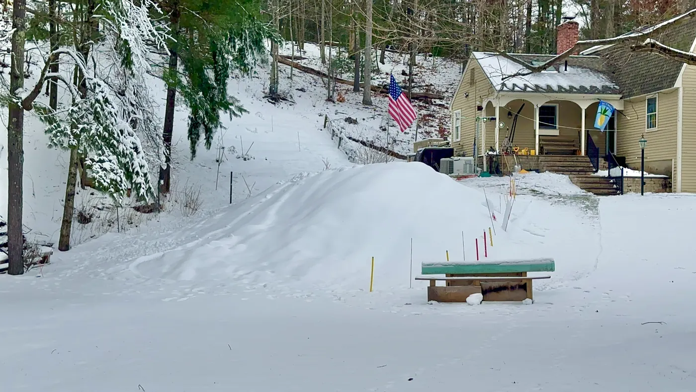 A snow-covered yard with a small feature in front of a house.
